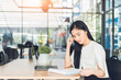 © kenchiro168 - Young business woman reading a report her hand holding a pen sitting in a coffee shop and working on laptop.