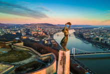 Budapest, Hungary - Aerial Skyline View Of Statue Of Liberty With Buda Castle Royal Palace And Chain Bridge At Background. Morning Sunrise With Blue Sky And Clouds