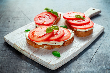 Wall Mural - Bruschetta, toast with soft cheese, basil and tomatoes on a white wooden board. Italian healthy snack, food.