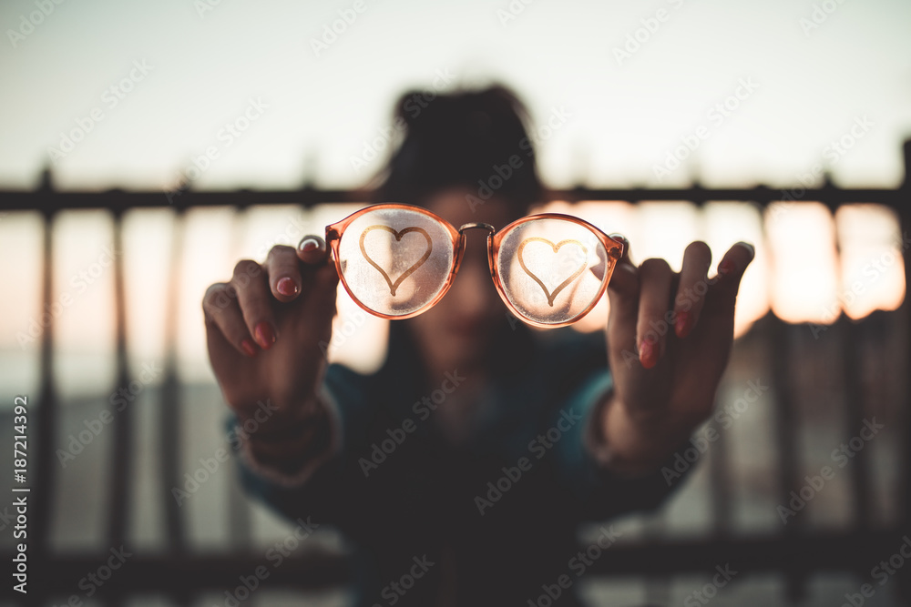 Simbolo del Cuore sugli occhiali di vetro appannato tenuti in mano da una ragazza. - obrazy, fototapety, plakaty 
