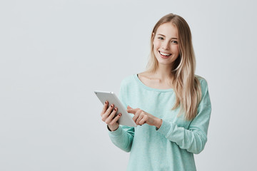 Wall Mural - Portrait of happy young blonde business woman in casual clothes using tablet isolated against gray background. Smiling pretty girl holding a digital tablet computer. Modern technologies and business