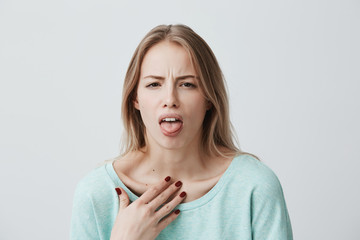 Wall Mural - Dissatisfied blonde female model frowns face, has disgusting expression, shows tongue, expresses non-compliance, irritated with somebody, rejects do something. People and negative facial expressions