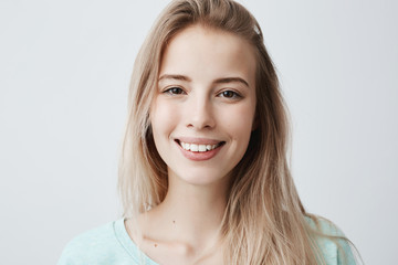 Wall Mural - Pleasant-looking woman with dark eyes, beautiful lips and pure skin looking with smile at camera rejoicing her vacation, relaxing. Positive female with long blonde hair posing against gray wall