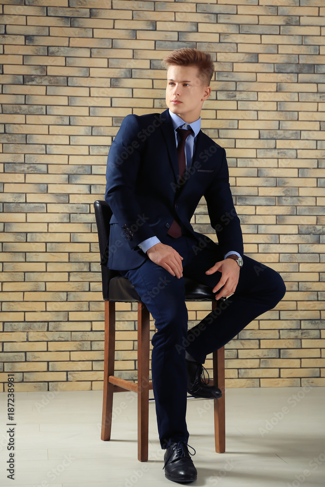 Handsome man in formal suit sitting on chair against brick wall