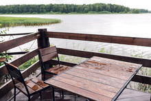 Cottage In Forest Near River With Big Wooden Terrace. House On The Water At The Lake, A Beautiful Bank. Ideal Place For Vacation And Holiday. Rain Drops On Table And Chairs