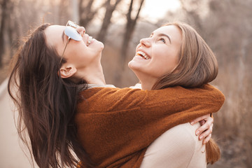 Two cute young women are hugging and laughing outdoors