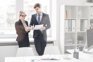 Wall Mural - Portrait of two successful business people man and woman, discussing work standing at window in modern office behind glass wall, copy space