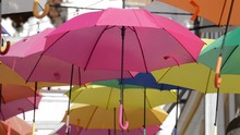 Pink Umbrella Hanging In A Village Square With Color Umbrella Heap
