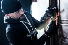 Lock. Determined Professional Bearded Burglar Holding A Torch And Wearing Gloves And Unlocking The Door