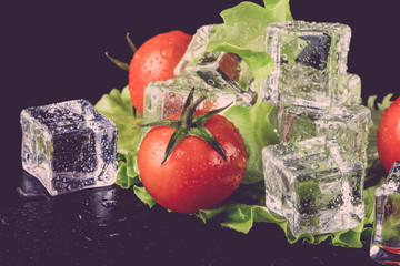 Wall Mural - Banch of red cherry tomatos, green salad and ice cubes on black wet table. Selective focus. Toned