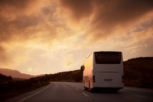 White Bus Driving On Road Towards The Setting Sun