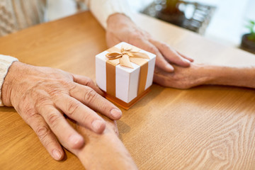 Wall Mural - Loving senior couple holding hands while sitting at cafe table and exchanging Christmas presents, close-up shot