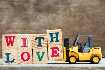 Wall Mural - Yellow toy forklift hold letter block H and E to complete word with love on wood background