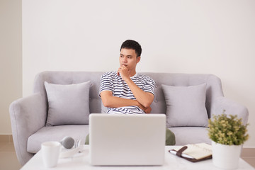 Young man looking up while working on laptop at home