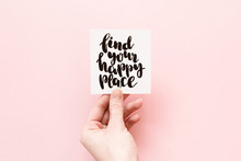 Minimal Composition On A White Background With Girl's Hand Holding Card With Inspirational Quote "find Your Happy Place" Written In Calligraphy Style