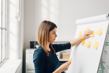 Young woman sticking sticky notes to flip chart