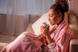 © Yakobchuk Olena - Serene african girl is drinking tea with pleasure. She is sitting on couch at home in cozy atmosphere