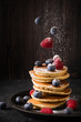 Homemade pancakes stack with sugar, strawberries and blueberries over dark texture. levitation