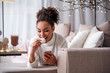 © Yakobchuk Olena - Portrait of cheerful african girl eating zephyr with enjoyment. She is lying on couch and looking at mobile phone with interest. Home relaxation concept