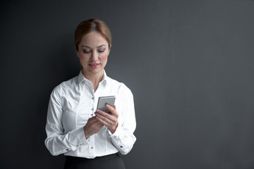 Poster - Portrait of smiling lady looking at screen of mobile while leaning against wall. Business concept. Copy space