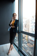 © Yakobchuk Olena - Full length portrait of smiling businesswoman telling by mobile while standing near window. She keeping document in hand. Communication and work concept