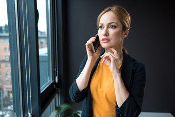 Poster - Portrait of thoughtful female speaking by mobile while looking at window in apartment. Conversation concept