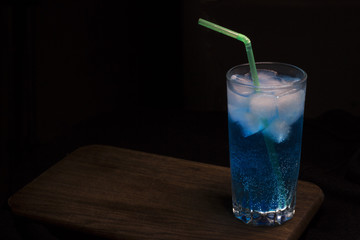 Blue cocktail with ice on wooden deck on dark background