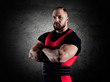 The weightlifter stands in a menacing pose with crossed huge arms