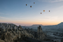 Colorful Hot Air Balloons Above Rugged Desert Landscape At Sunrise, Cappadocia, Turkey