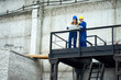 © Seventyfour - Wide angle portrait of two female workers standing at metal balcony and inspecting construction plans, copy space