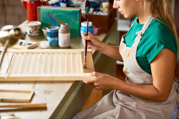 Canvas Print - Side view of blonde young woman enjoying work in art studio painting shutters with bronze paint, making DIY interior decorations