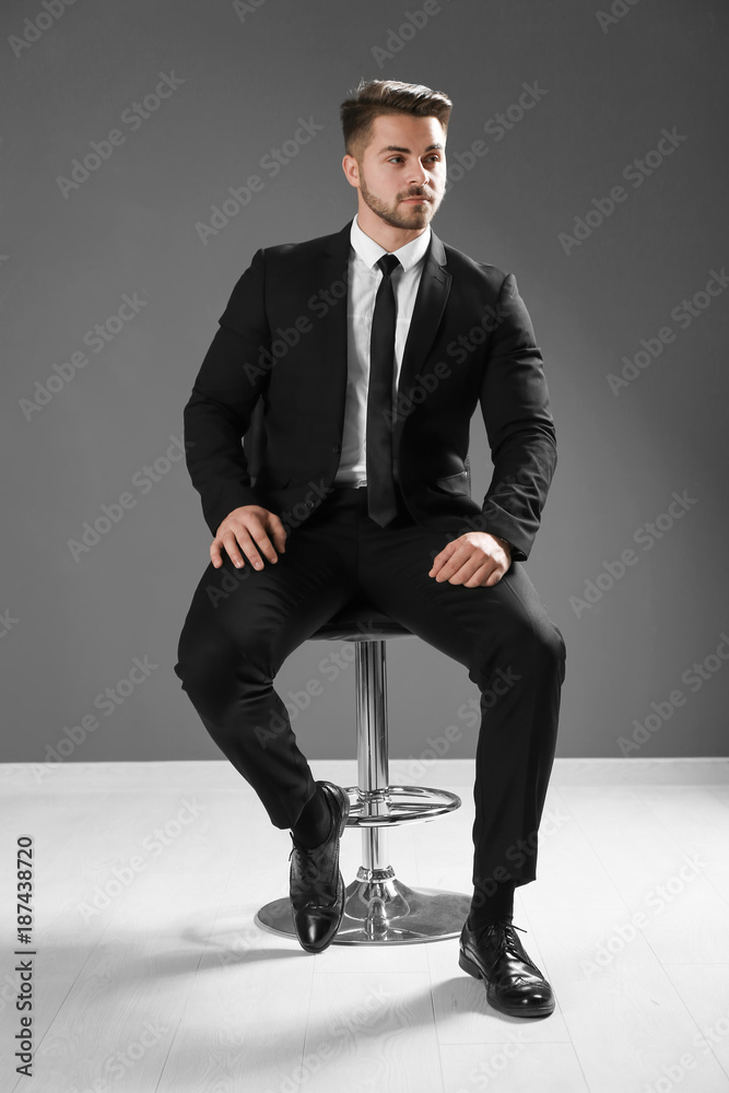 Handsome man in formal suit sitting on chair against grey wall