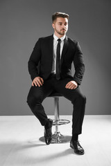 Poster - Handsome man in formal suit sitting on chair against grey wall