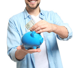 Man putting money into piggy bank on white background