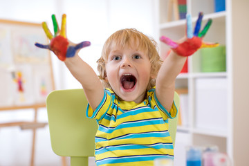 Wall Mural - Paint fingers, child boy drawing with hands and showing multi-colored palms.