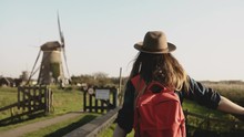 Local Girl Slowly Walks Up To A Windmill Farm. Woman In Hat With Long Hair And Red Backpack Coming Back Home. 4K.