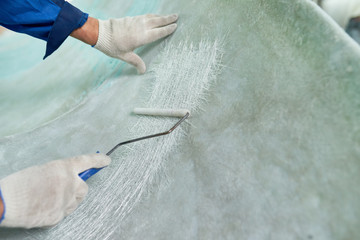 Close up of workers hands repairing boat  in yacht workshop, covering boat with pre-paint base coating,  copy space