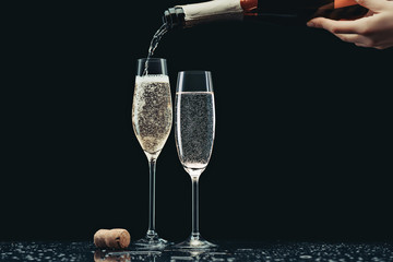 Wall Mural - cropped image of woman pouring champagne from bottle into glasses on black