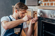 © LIGHTFIELD STUDIOS - handsome young repairman fixing oven with screwdriver