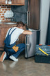 © LIGHTFIELD STUDIOS - back view of repairman in protective workwear fixing refrigerator in kitchen