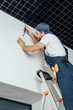 © LIGHTFIELD STUDIOS - low angle view of young electrician standing on ladder and fixing home alarm