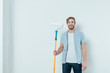 © LIGHTFIELD STUDIOS - handsome young man holding paint roller and smiling at camera on grey