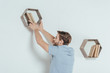 © LIGHTFIELD STUDIOS - young man hanging wooden shelf with books at home