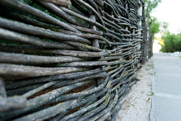 a wicker fence, a decorative fence, a wattle fence, branches, lath fence, in the background of a path made of stone and green bushes