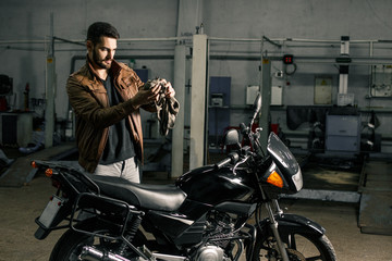 Wall Mural - Young man in leather jacket standing near motorcycle in garage