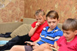 © andov - Four children, slouching on a couch in a living room, gaming on tablets and smart phones, being bored