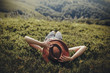 stylish traveler woman in hat lying on grass and relaxing in mountains. hipster girl on top of mountain, resting, hat on her face. space for text. atmospheric moment. wanderlust and travel concept.