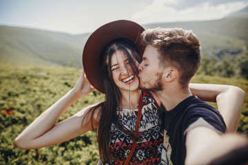 Sticker - wanderlust and travel together concept. stylish couple travelers in hat making selfie at mountains. hipster family smiling and kissing on top of mountain. space for text. atmospheric moment