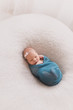 © Lea Csontos/Stocksy - Cute newborn baby sleeping swaddled in a blue knit blanekt