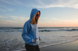 © Carolyn Lagattuta/Stocksy - Young woman standing on beach in hoodie and heart shaped sunglasses